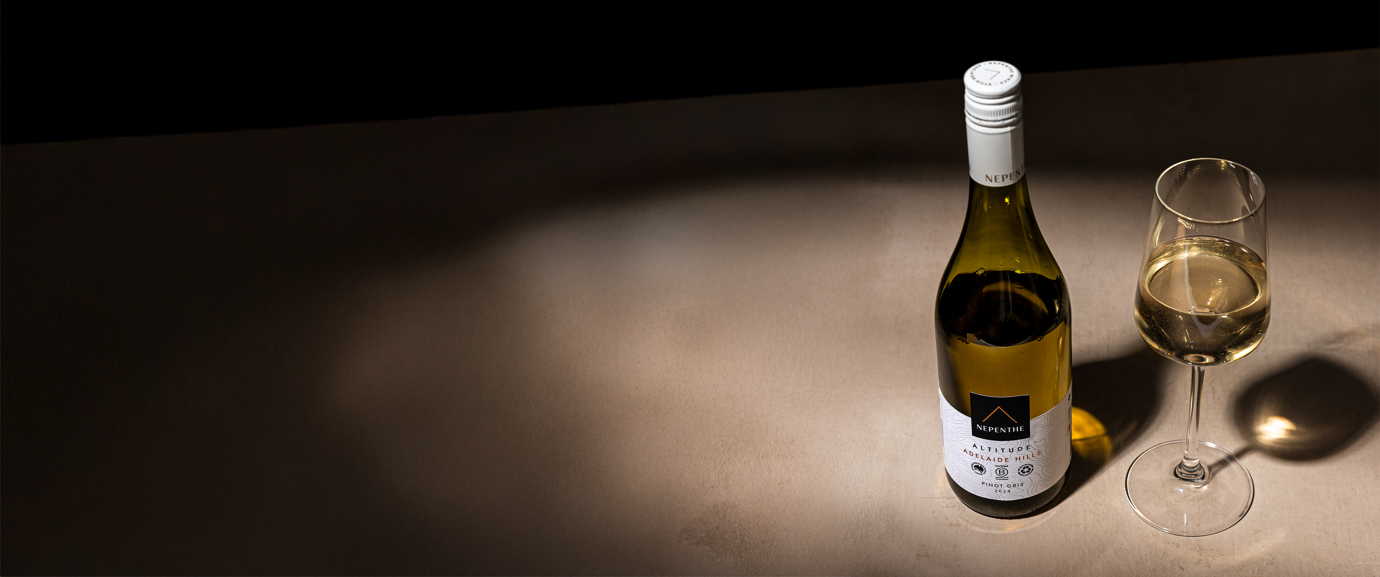 Nepenthe Altitude Chardonnay stood next to a wine glass full of wine with a dark fade in the foreground.