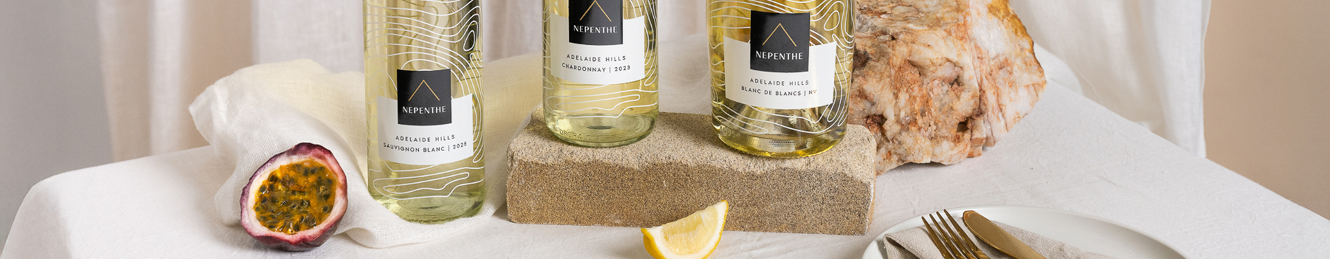 Nepenthe Ascend range bottles on a table with a white table cloth, cutlery and a plate with passionfruit and a lemon wedge.